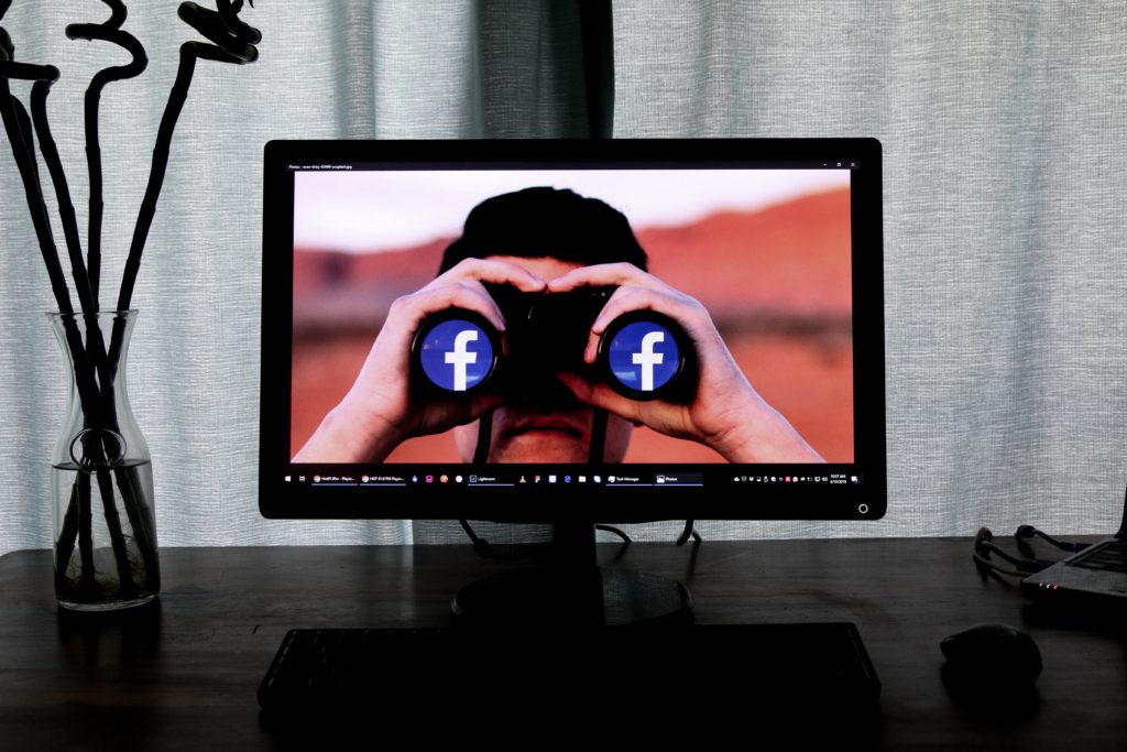 Man with binoculars on screen with Facebook logos for lenses